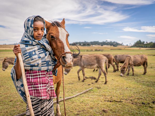 A young girl and her horse stand in a field in Ethiopia.