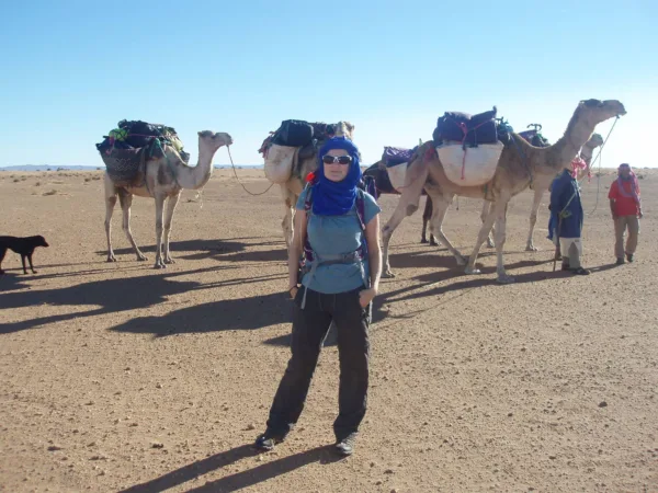 A lady stands in front of three camels in the Sahara Desert as she participates in a trek to raise funds for SPANA.