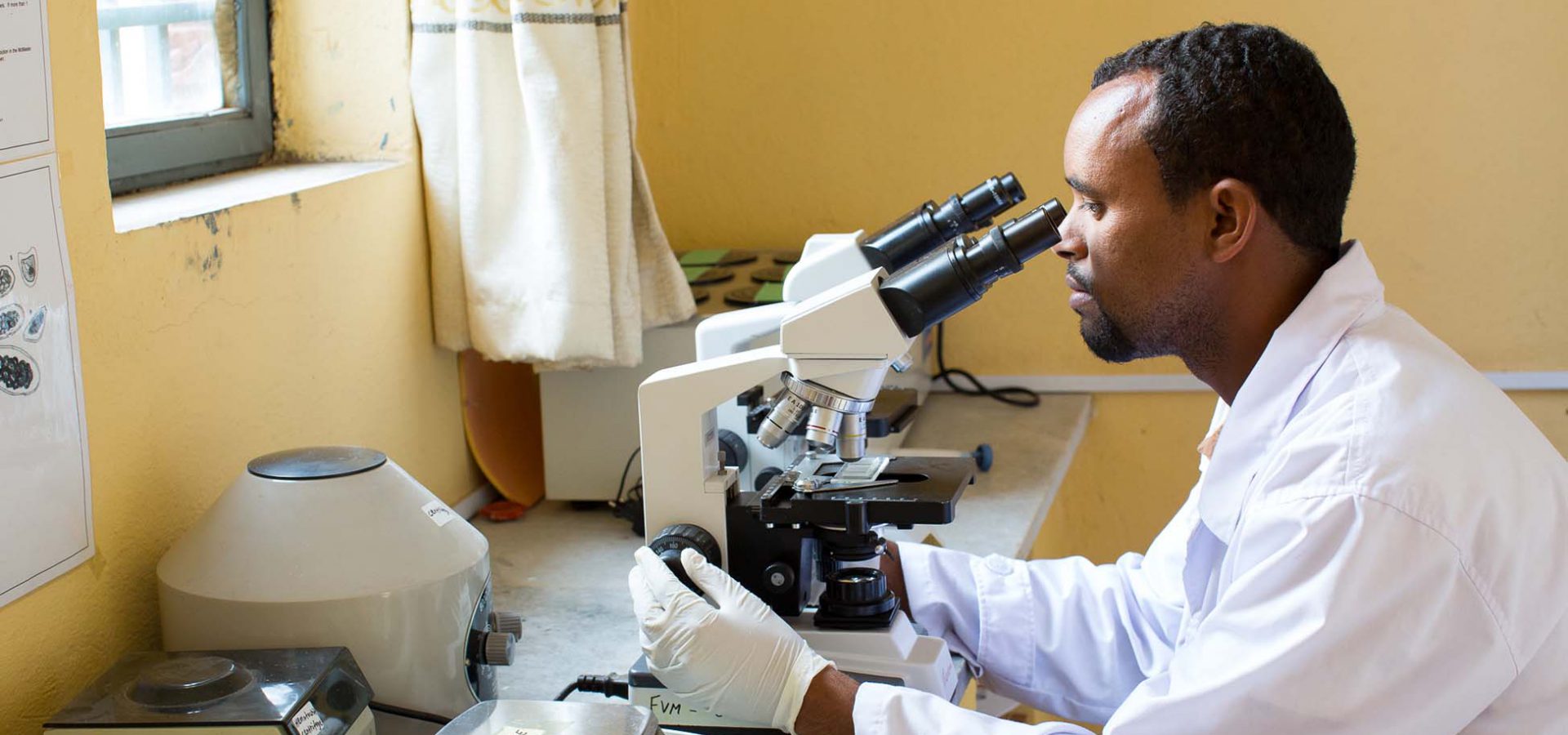 Man in white coat looking through microscope