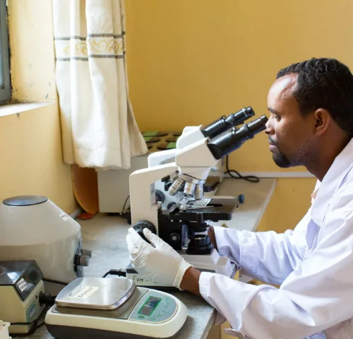 Man in white coat looking through microscope