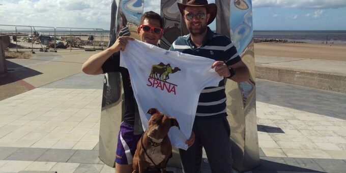 Two men are smiling as they pose with a dog and a SPANA shirt.