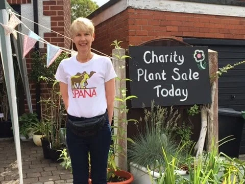 A lady wearing a SPANA t-shirt stands next to a sign stating 'Charity Plant Sale Today'.