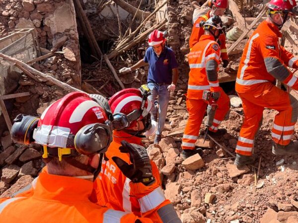 rescue team dressed in bright orange uniforms stand on mounds of rubble