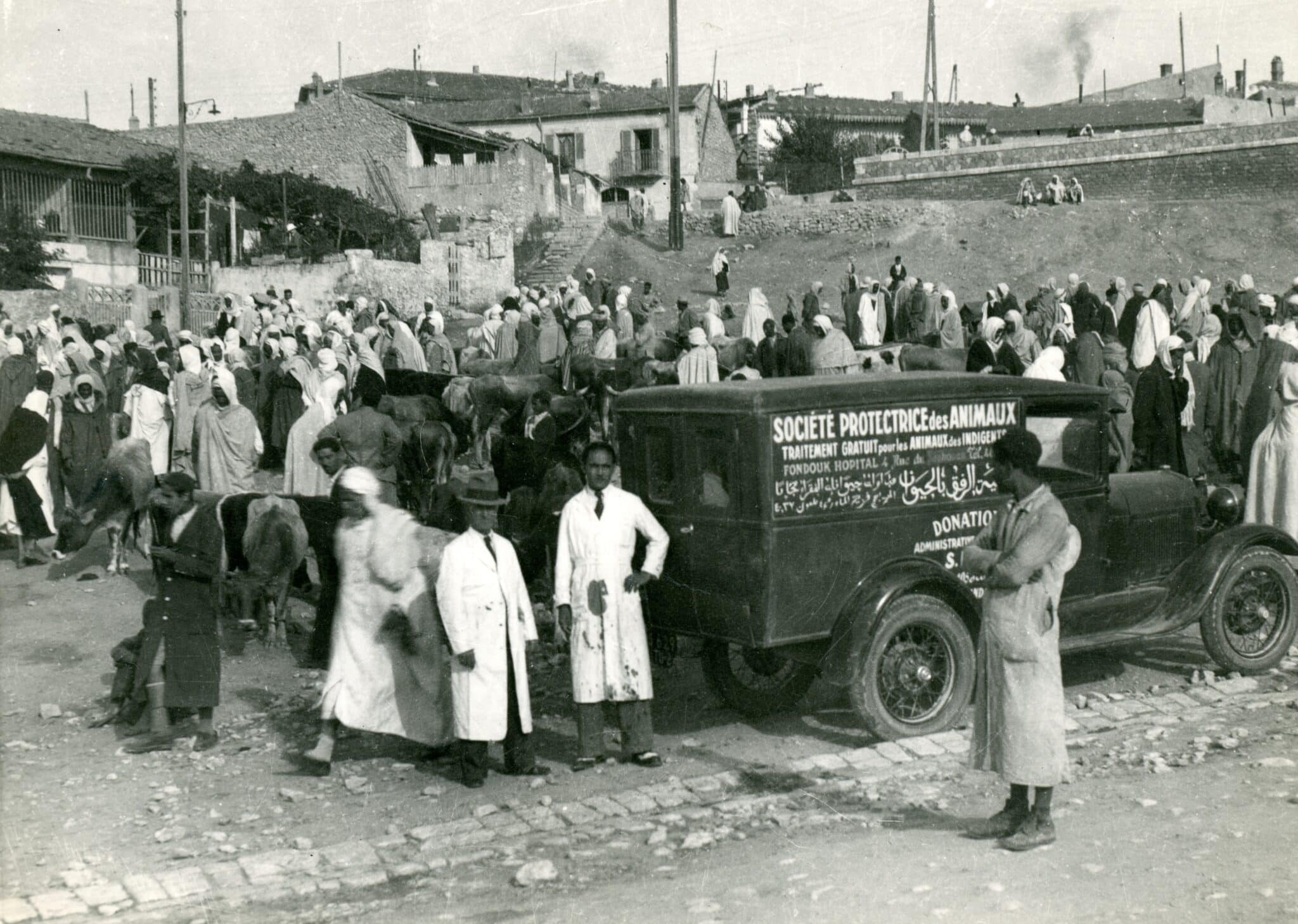 black and white image of SPANA's first mobile clinic, a ford, surrounded by a crowd of people