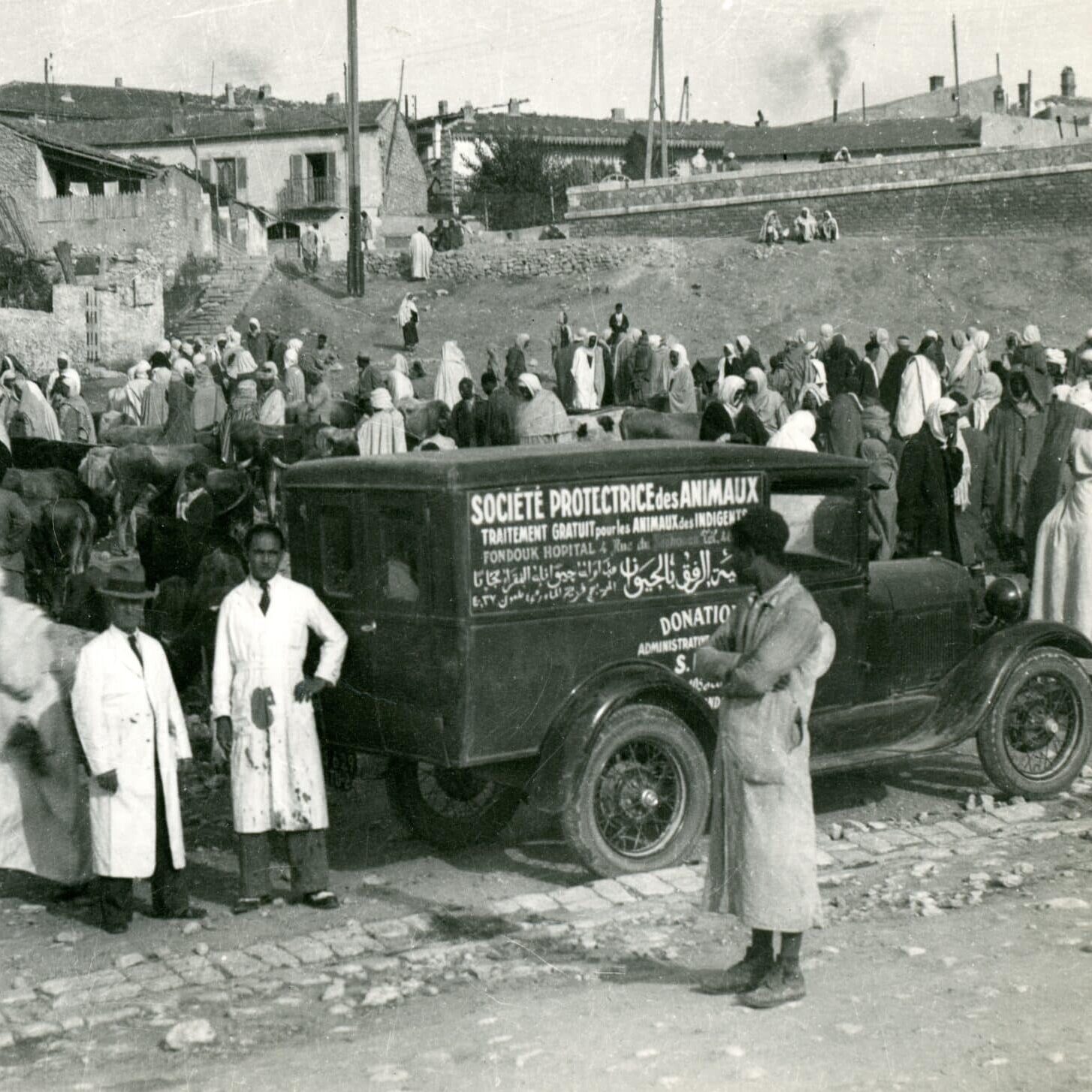 black and white image of SPANA's first mobile clinic, a ford, surrounded by a crowd of people