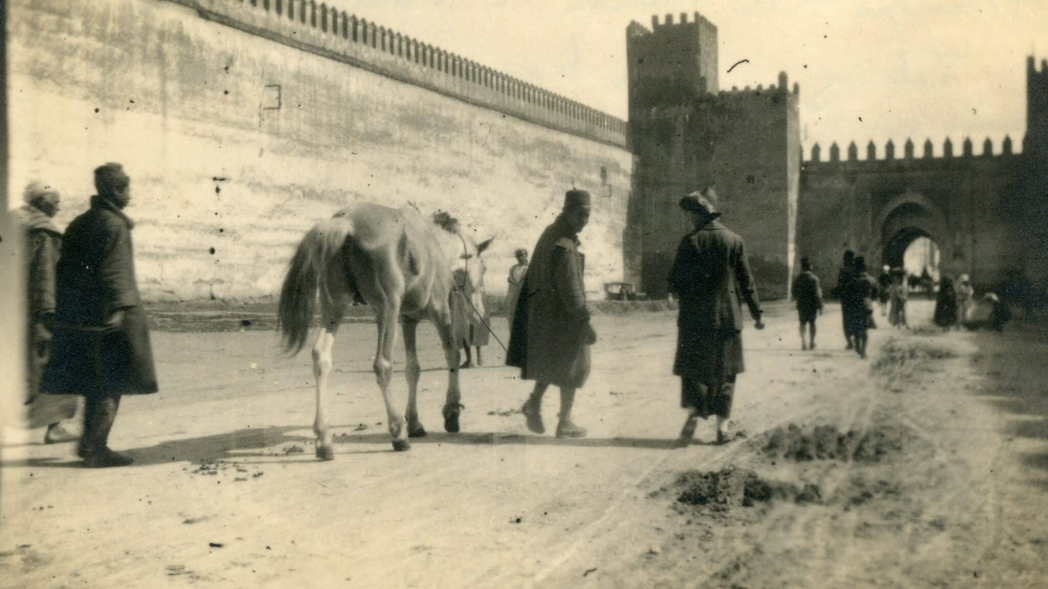 black and white photo of Kate Hosali, founder of SPANA, walking in Morocco with a man and a horse